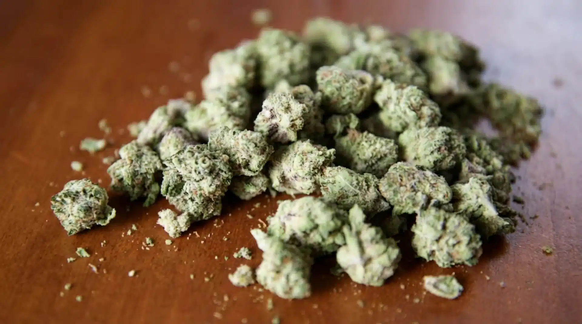 pile of cannabis buds scattered on wooden surface with visible crumbs, showing texture, color variation, and appearance