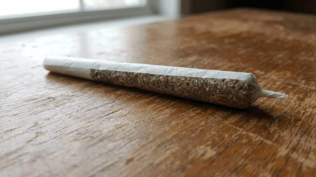 close-up of a hand-rolled spliff in white rolling paper resting on a wooden surface in natural daylight