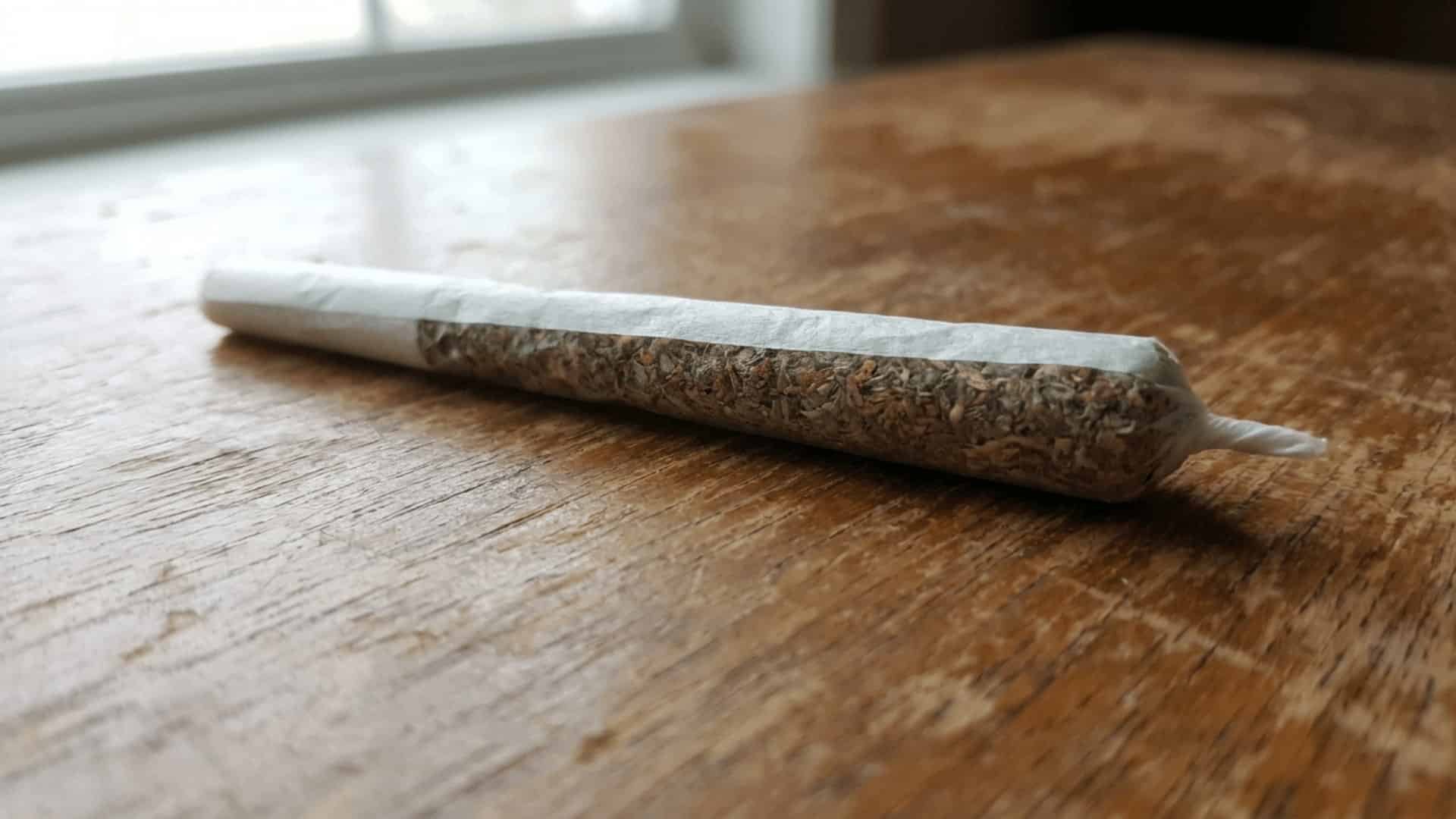 close-up of a hand-rolled spliff in white rolling paper resting on a wooden surface in natural daylight