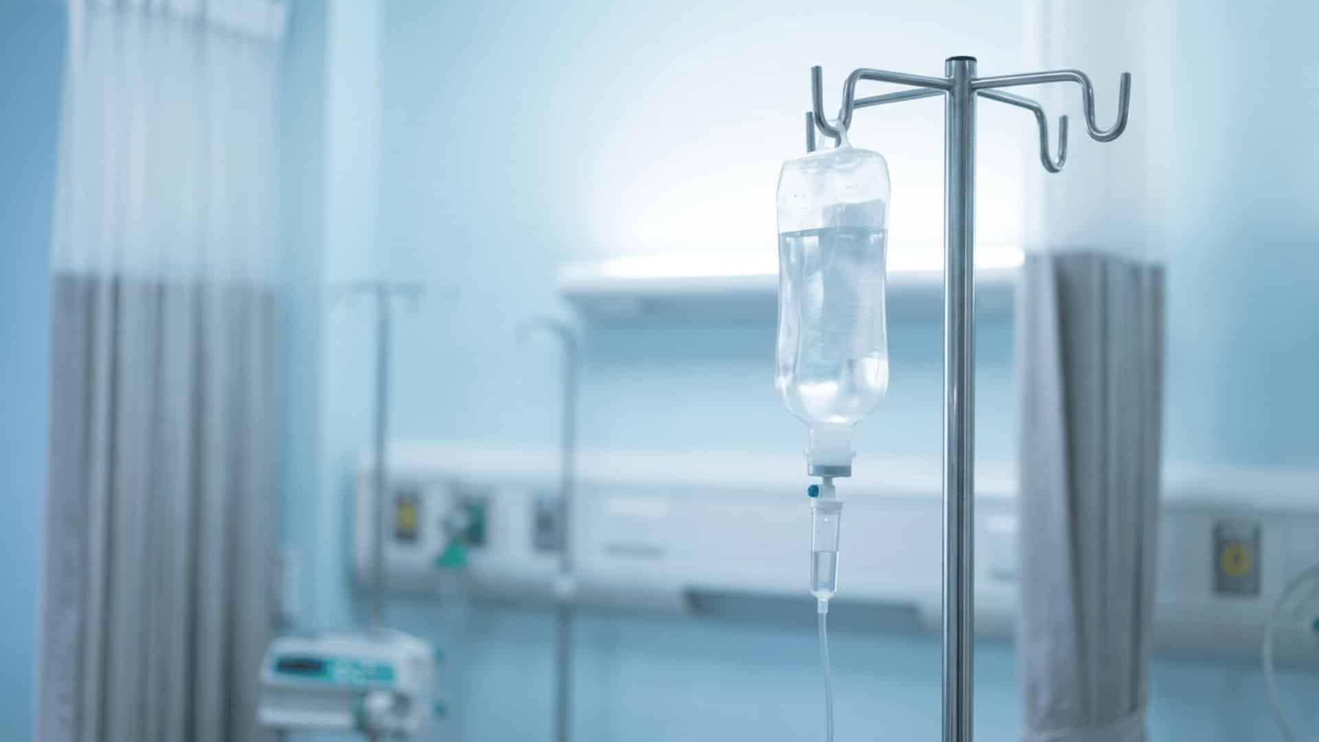 hospital iv drip stand with a clear fluid bag and tubing against a blurred sterile clinical background