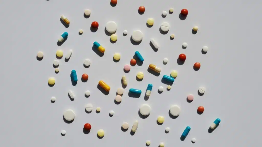 top down view of assorted white yellow blue and red pills and capsules scattered on a clean white background