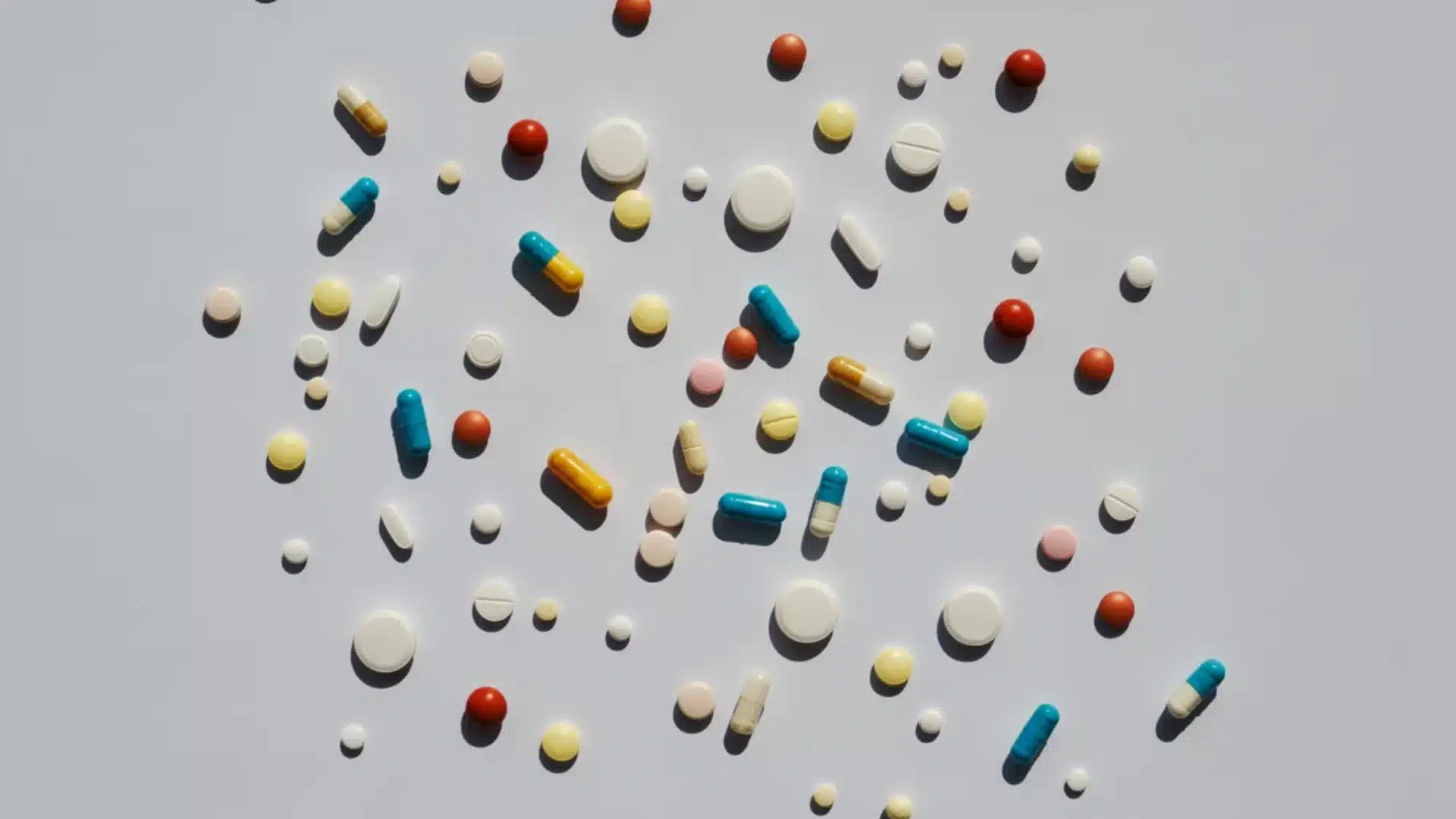 top down view of assorted white yellow blue and red pills and capsules scattered on a clean white background