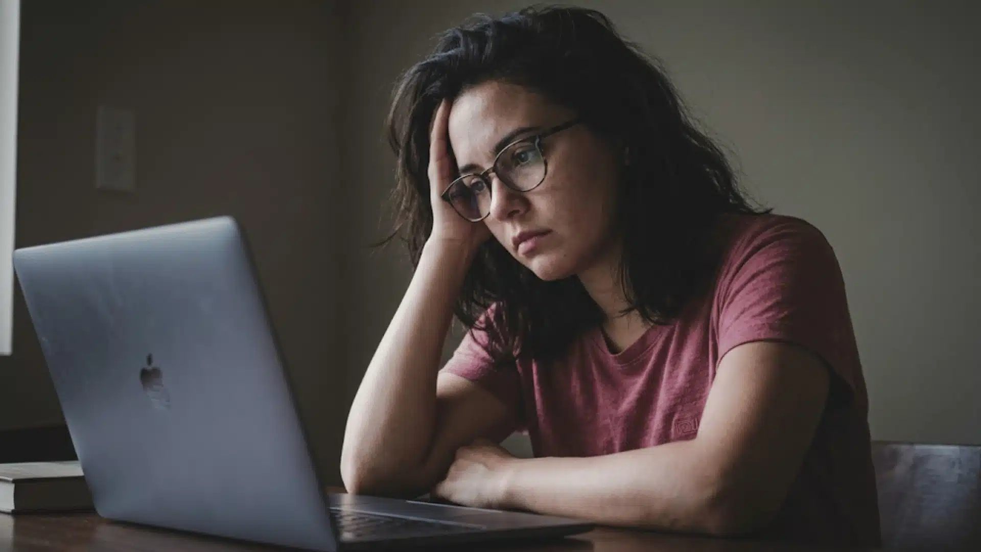 a woman sitting in front of laptop lop depressed and stressed in pink tshirt