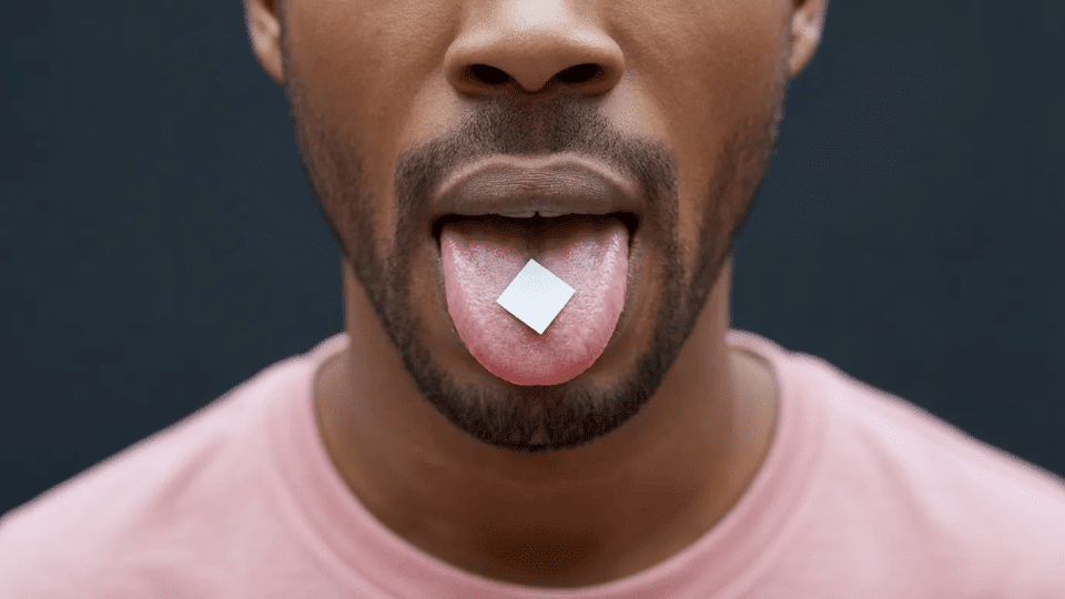 person with tongue out holding a small paper tab on the tongue close up