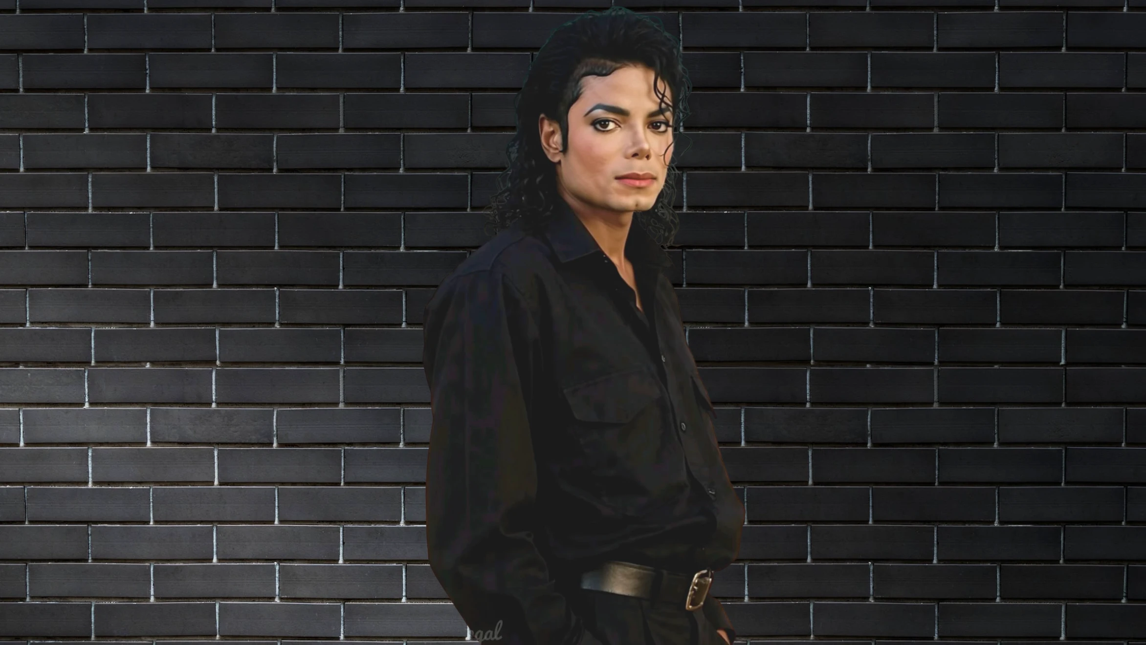 a man with curly hair, wearing a black shirt and belt, poses confidently in front of a black brick wall