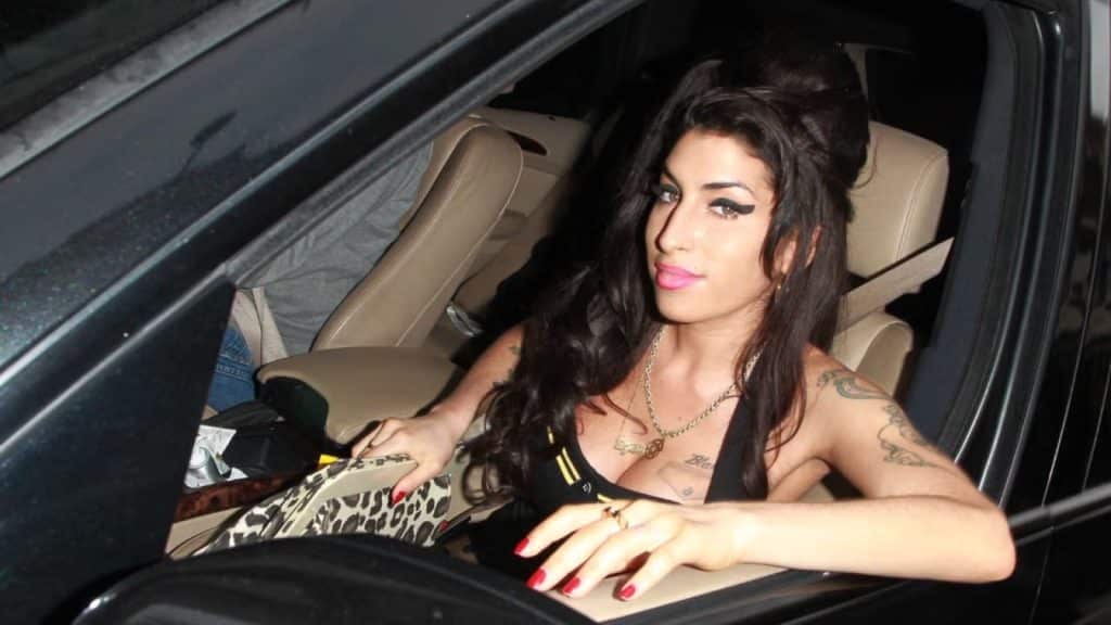 amy winehouse sitting inside a car at night with heavy eyeliner dark hair and a calm expression