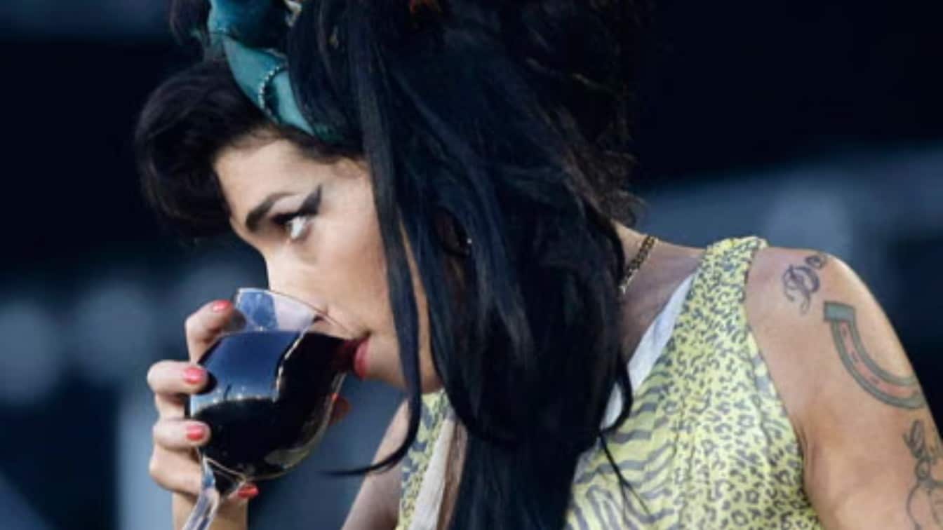 amy winehouse holding a glass while appearing at an outdoor event with dark hair and visible tattoos