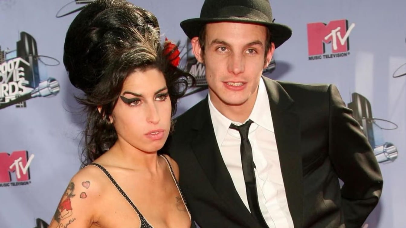 amy winehouse standing beside blake fielder-civil at a music awards event with a red carpet backdrop