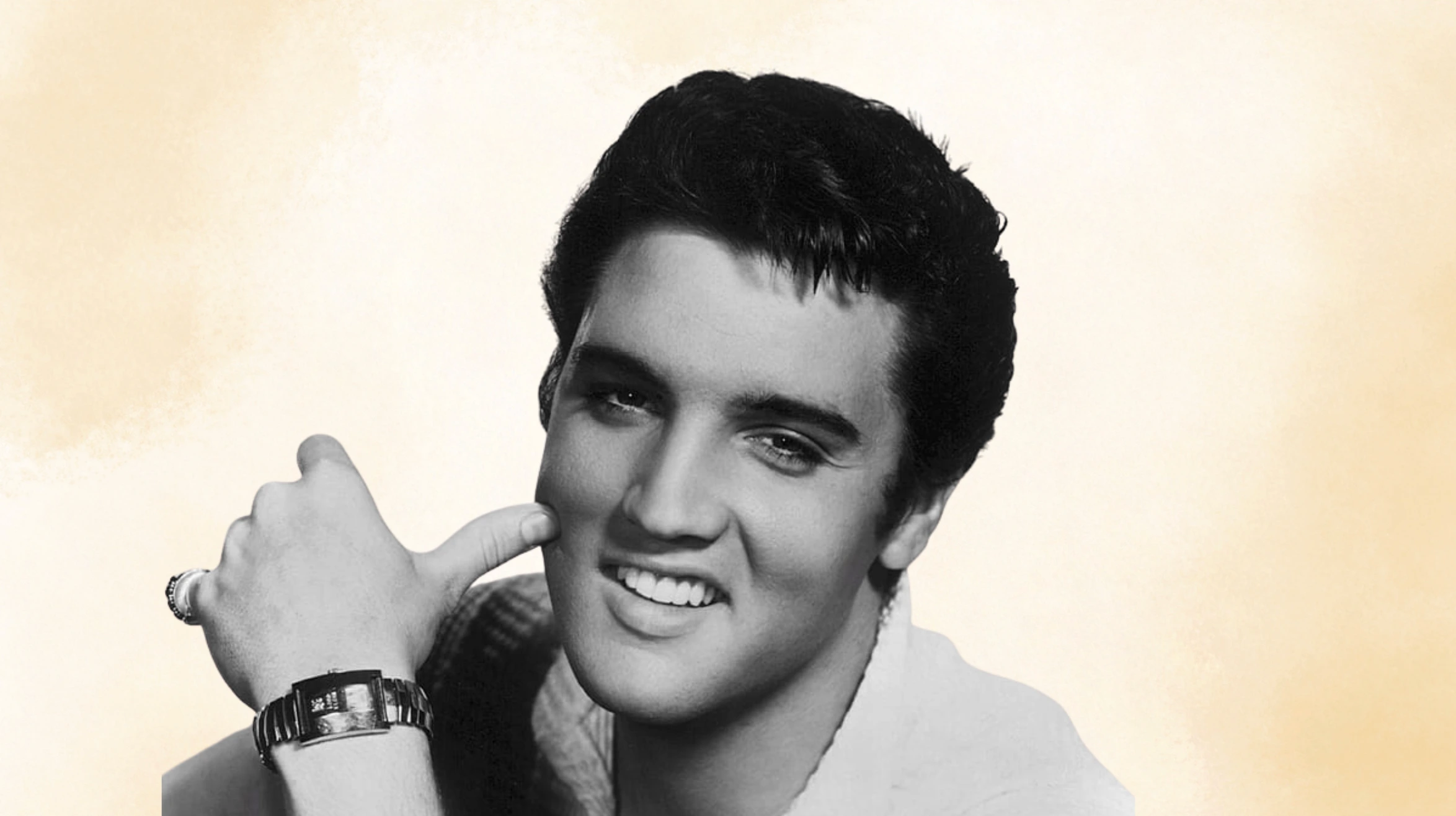 black and white portrait of man with dark hair, resting hand on cheek, wearing bracelet, against beige background