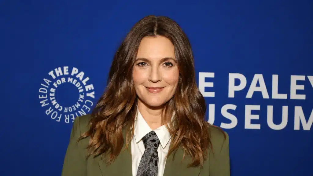 drew barrymore childhood portrait with olive green blazer, white shirt, patterned tie, and cobalt blue event backdrop