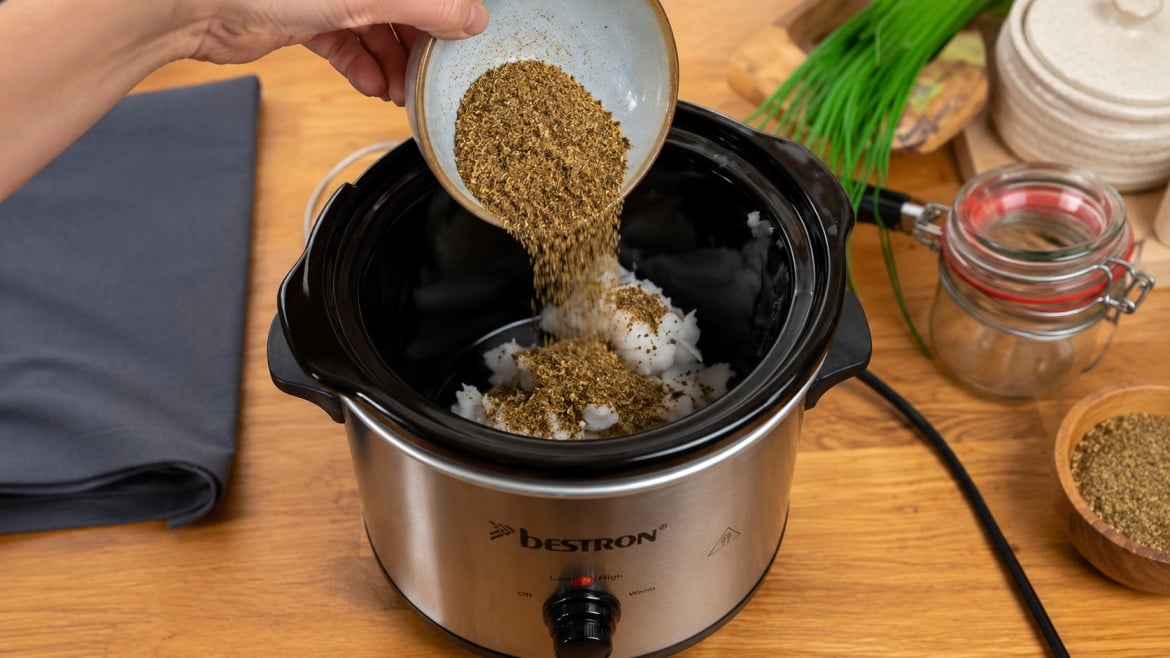 how to decarb weed with dried herbs poured into a slow cooker with white oil on a wooden kitchen counter