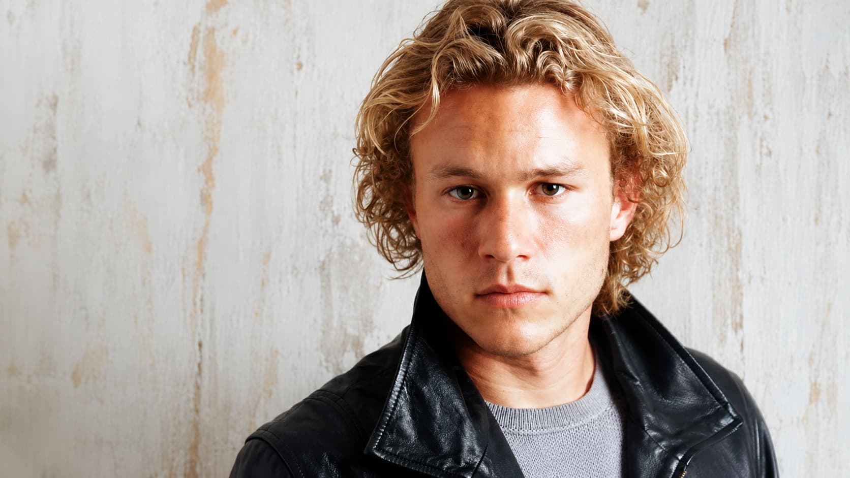 heath ledger in black leather jacket against a rustic white wall