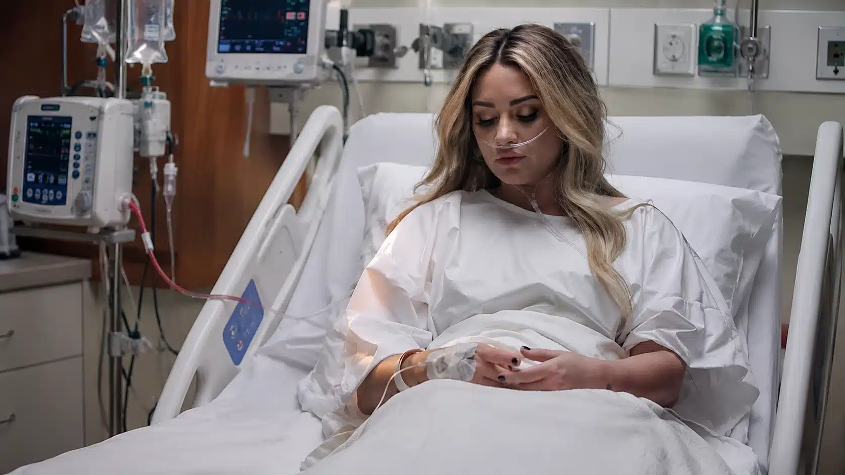 hospital scene showing demi lovato after overdose, with woman in bed, oxygen tube, iv line, monitors, in a clinical room