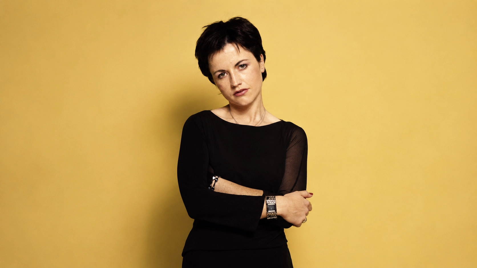 image for female singers who died of an overdose, showing a serious woman in black against a yellow wall