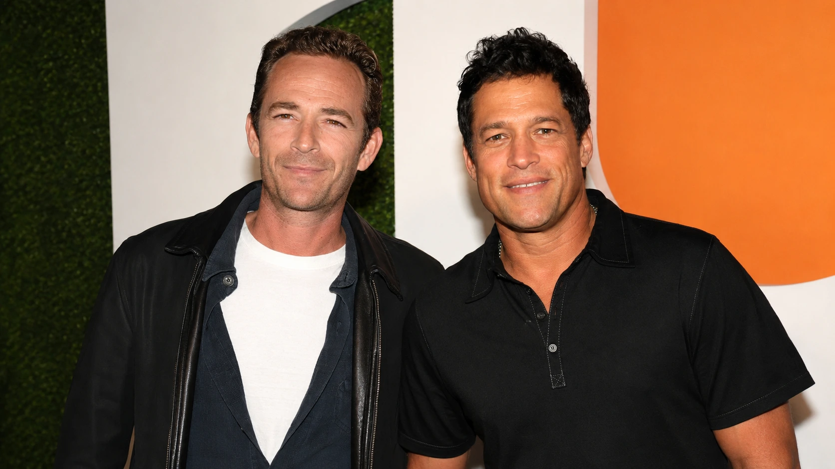 two smiling men stand close together for a natural event photograph against a white, green, and orange backdrop wall