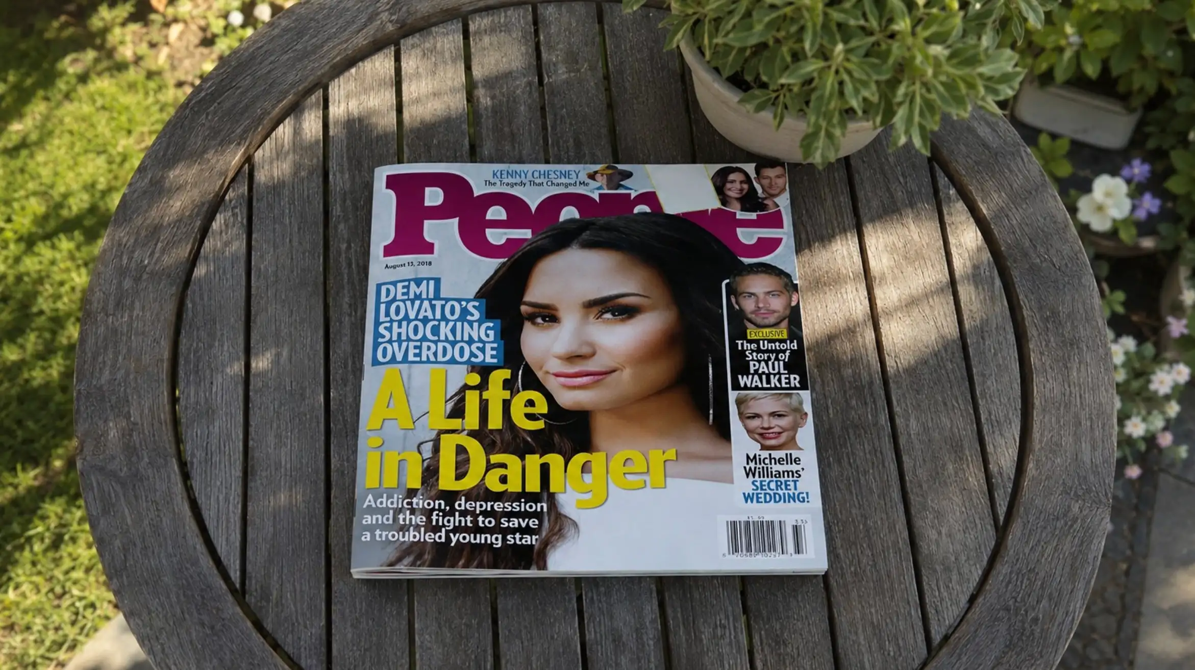 people magazine about demi lovato overdose rests on a round wooden garden table with plants and sunlight nearby