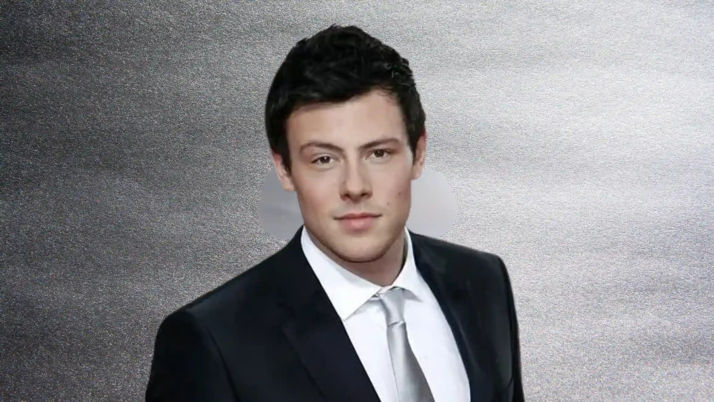 portrait of man in black suit and tie, short dark hair, facing camera against gray background with neutral expression