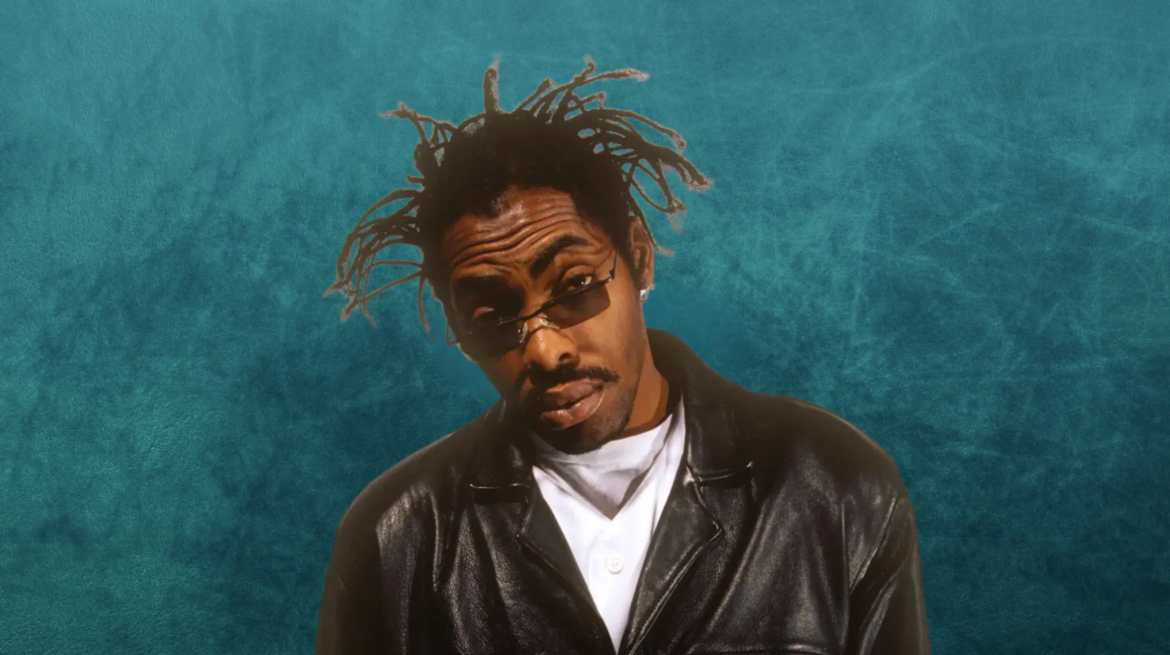 portrait of man with short dreadlocks wearing sunglasses and black leather jacket, tilting head against blue background