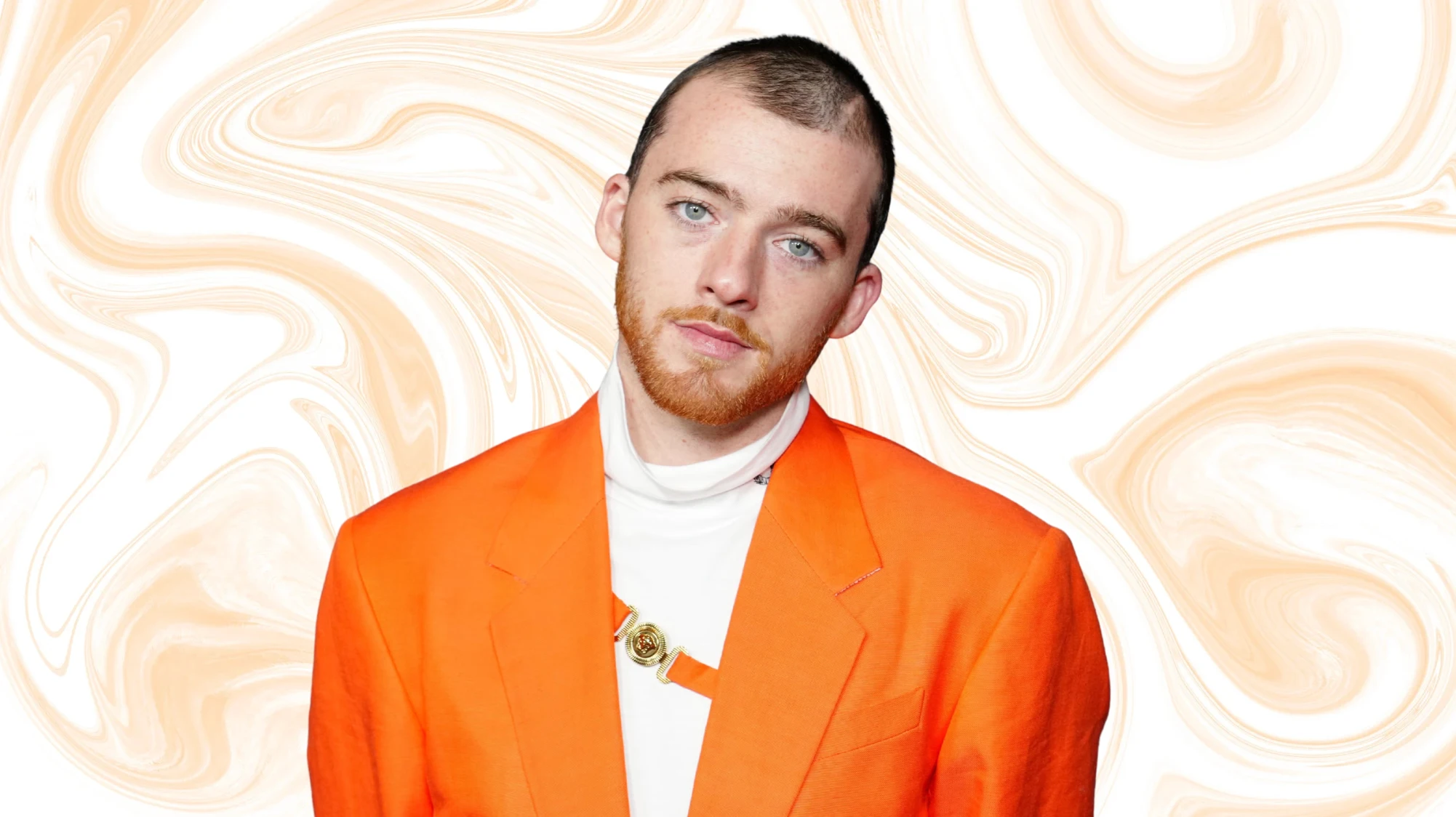portrait of man with short hair and beard wearing bright orange blazer, tilting head slightly, against beige background