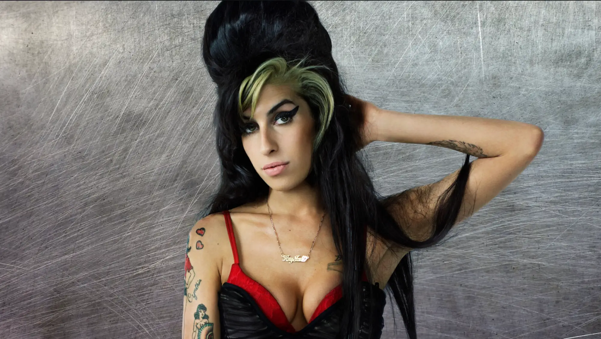 portrait of woman with dark beehive hairstyle and blonde streak, wearing red and black outfit, tattoos visible