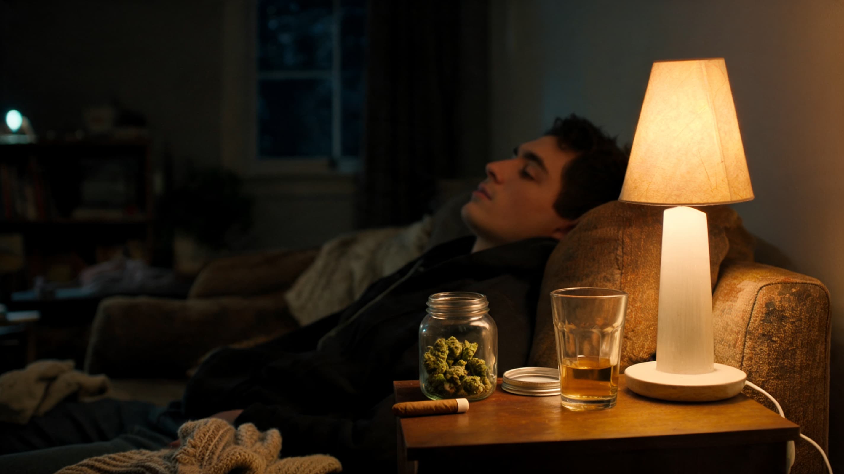 relaxed person sitting on couch in warm dim room showing cannabis calm effects