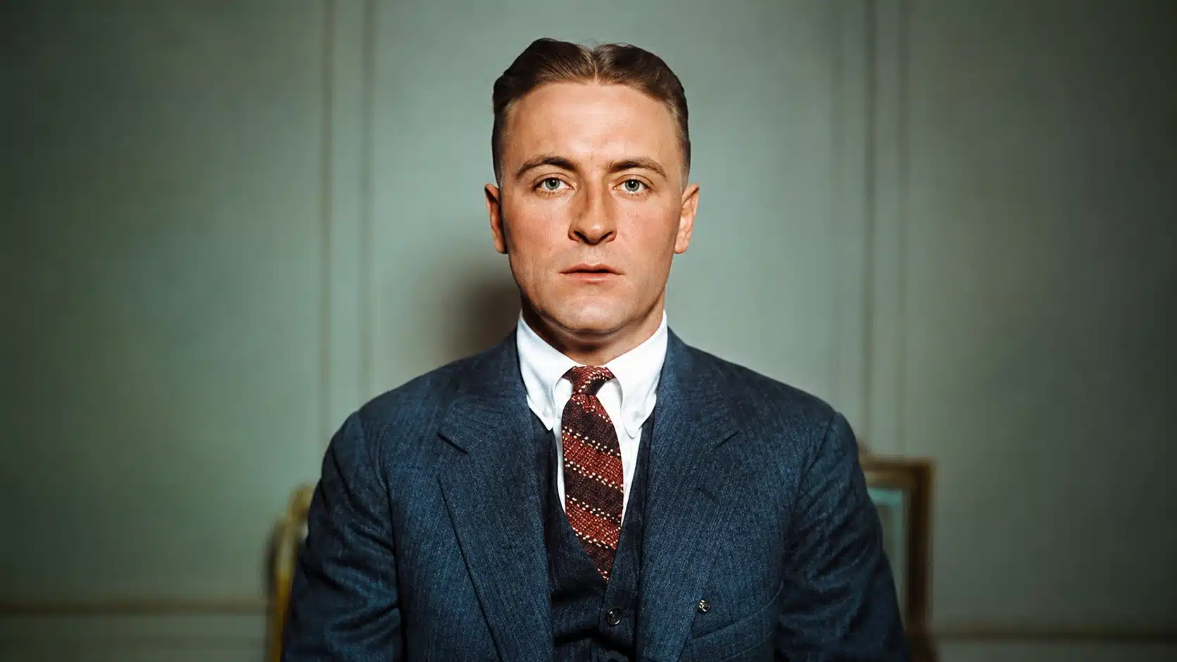 colorized vintage portrait of a serious man in a blue suit, red tie, and formal studio setting