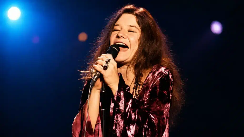 janis joplin performing on stage, singing into microphone under bright lights, representing janis joplin cause of death