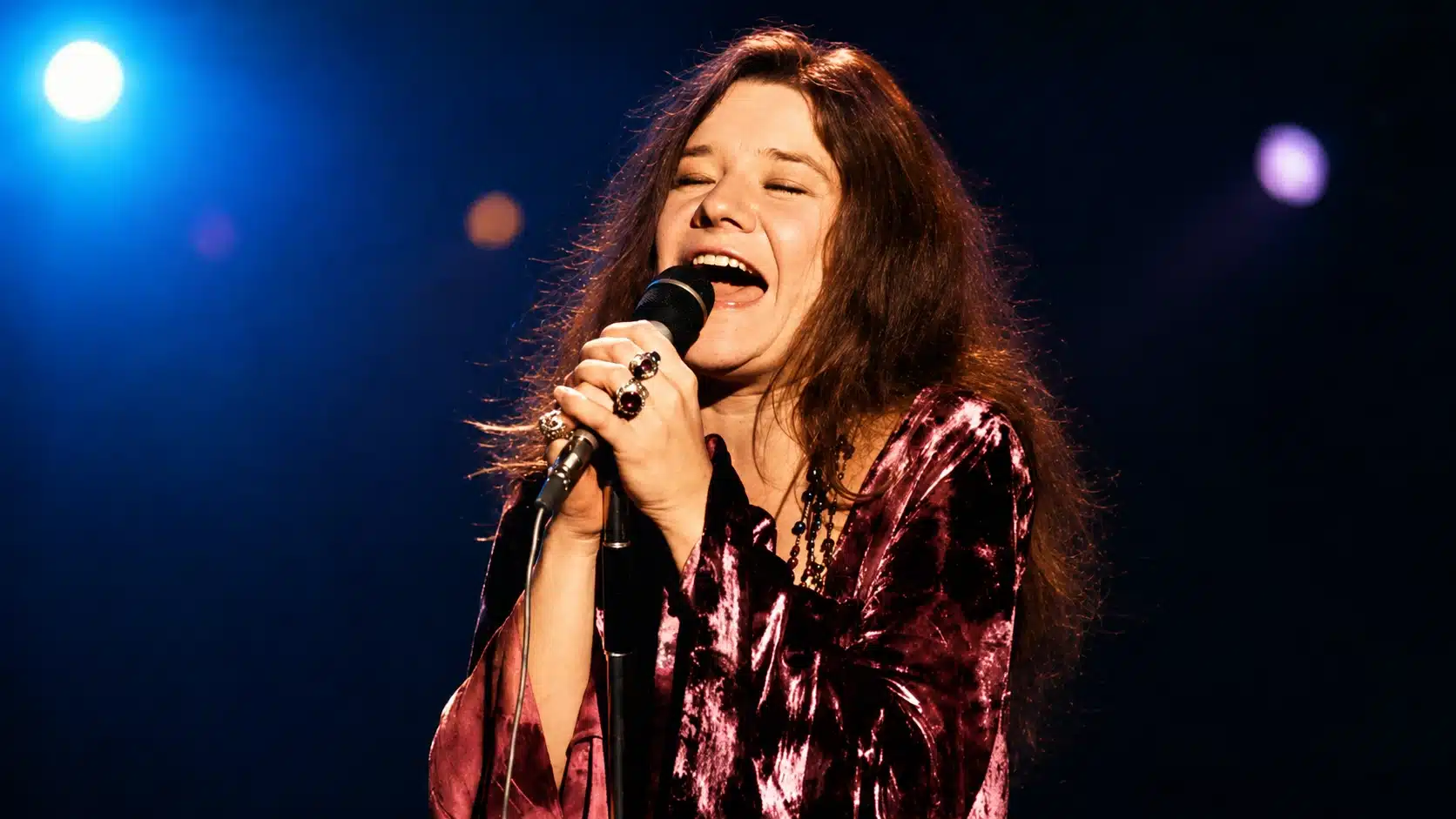 janis joplin performing on stage, singing into microphone under bright lights, representing janis joplin cause of death