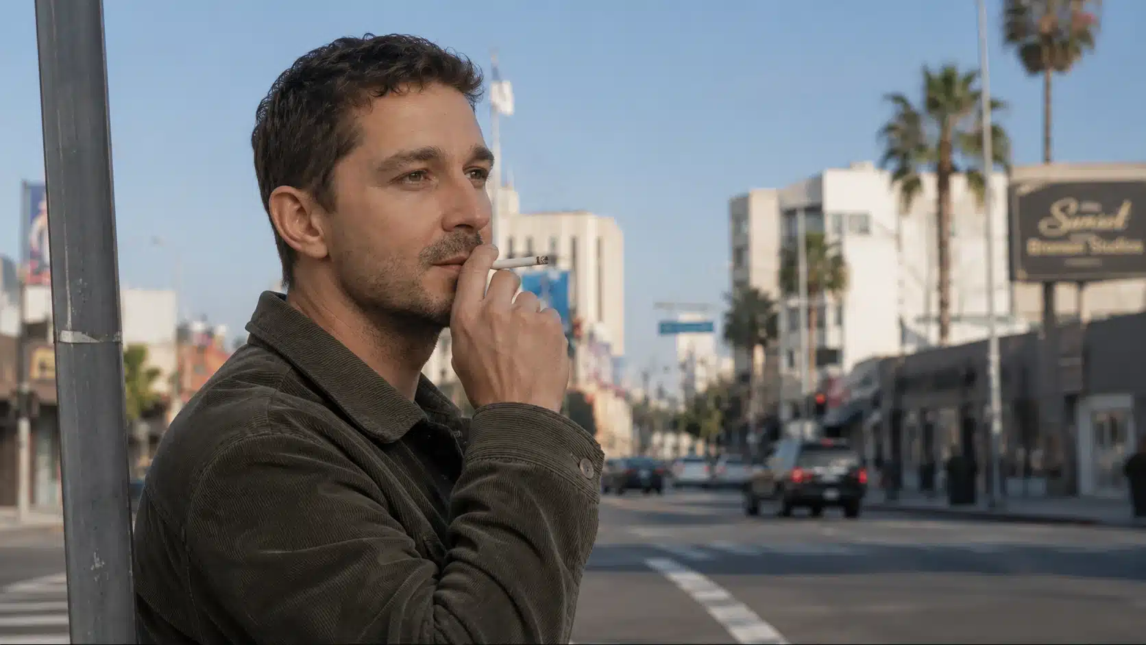 man smoking a cigarette from side angle on a sunny los angeles street, wearing a casual jacket near palm trees