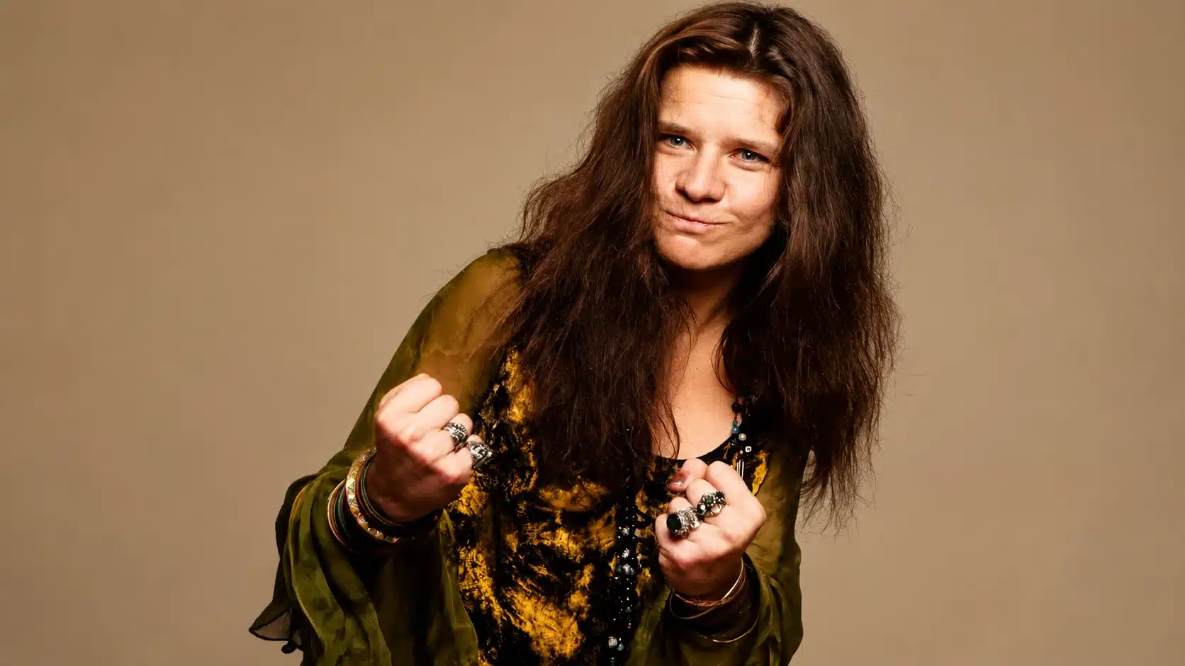 portrait of janis joplin with fists raised, wearing mustard and green outfit, relating to janis joplin cause of death