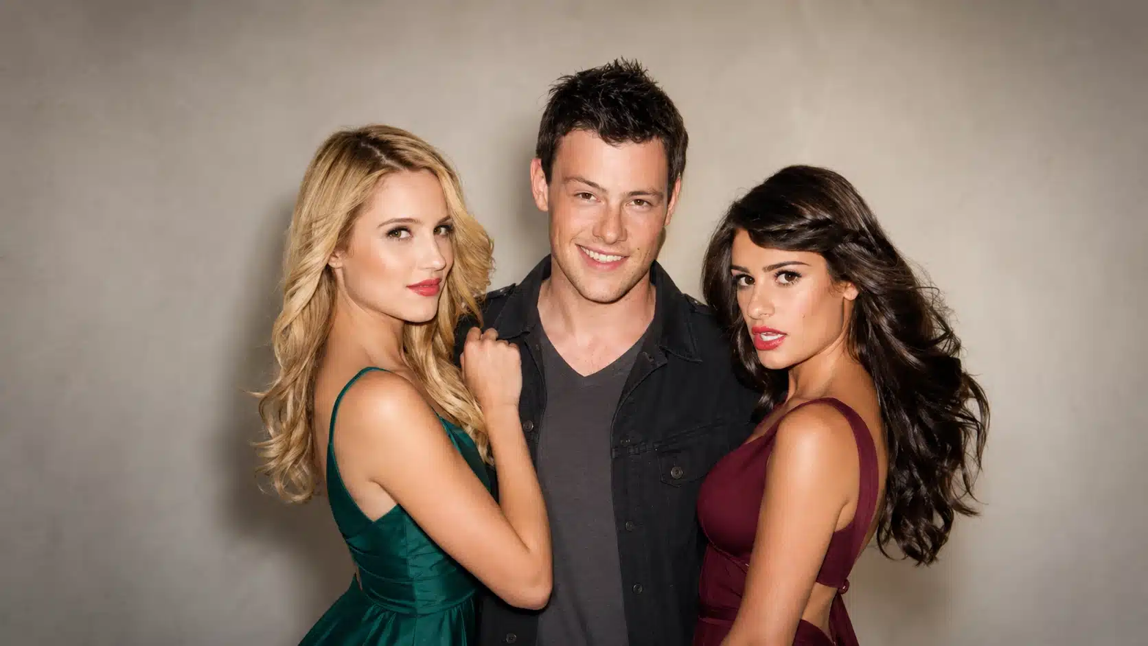 three stylish young adults pose together against a plain beige wall, wearing changed outfits, smiling confidently