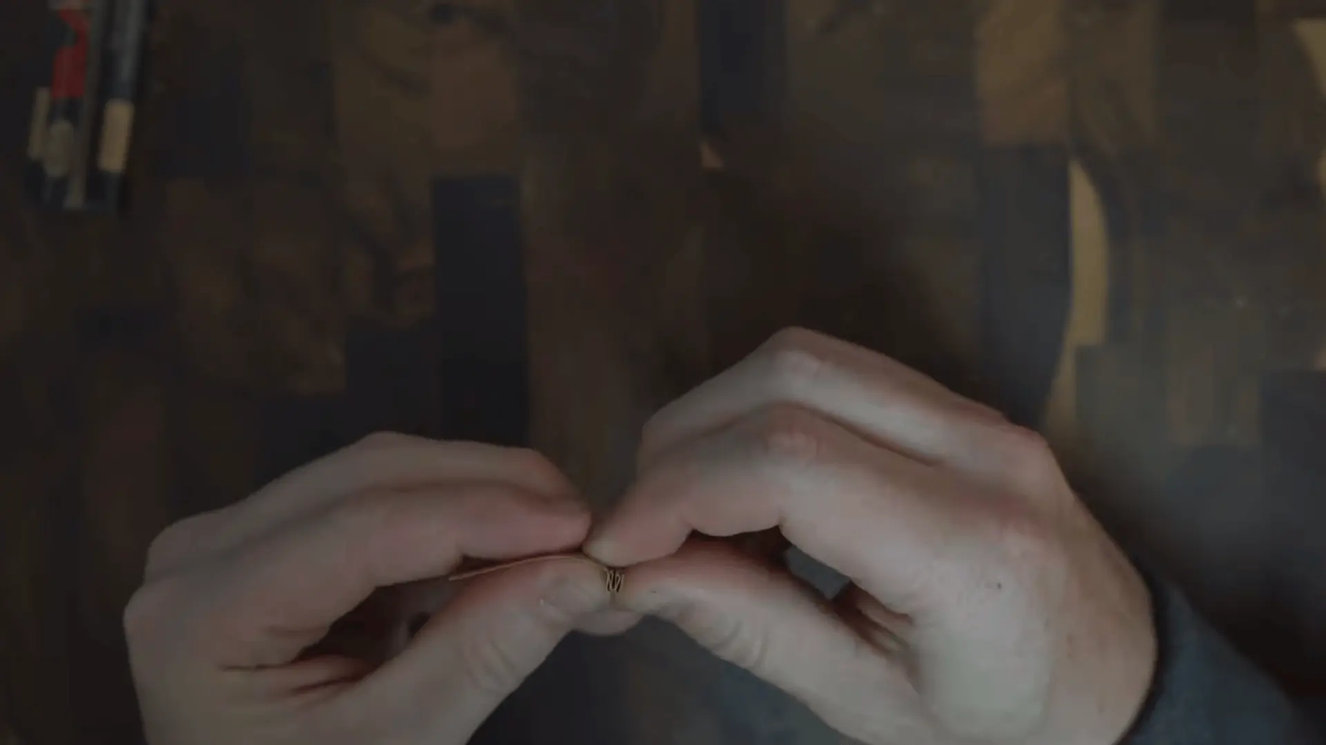 two hands pinch and shape a small rolling paper over a dark wooden tabletop during preparation