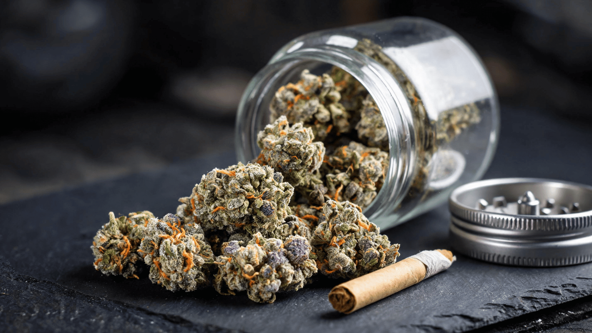 glass jar spilling frosty cannabis buds onto a dark surface