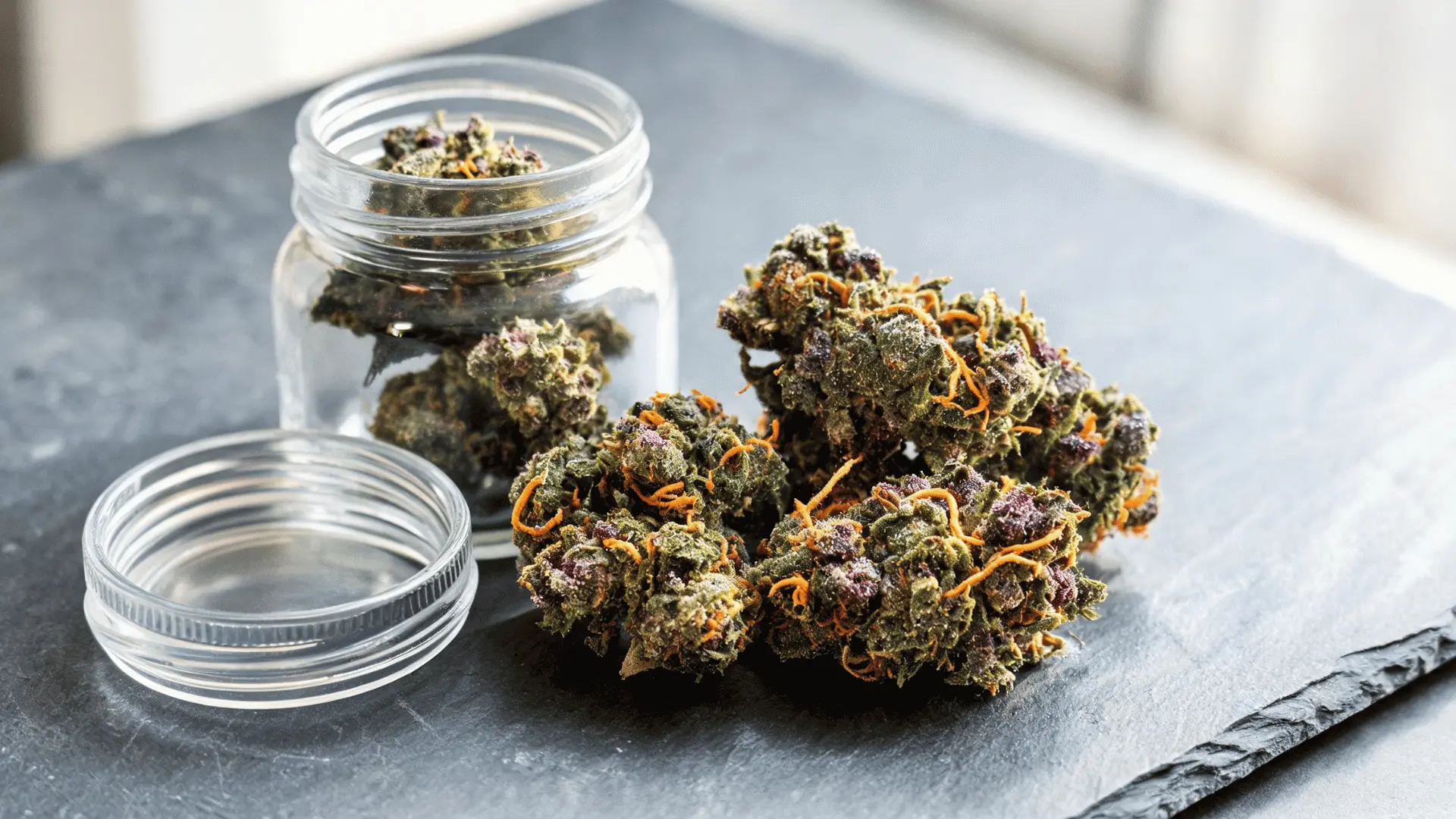 fresh frosty cannabis buds displayed beside an open jar on a clean surface